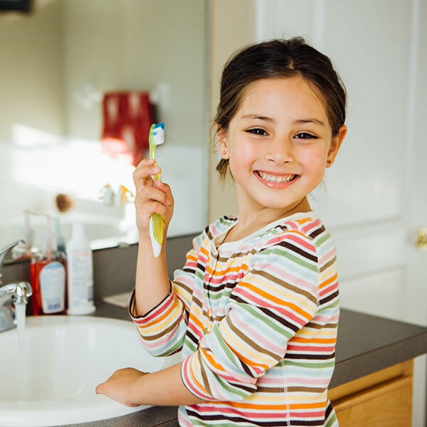 A little girl in front of a mirror brushing her teeth before her family dentistry appointment